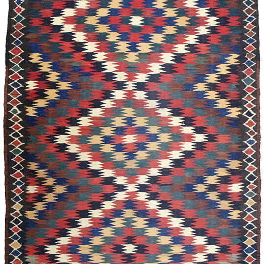 alt="Antique Varamin kilim rug with eye dazzler design from Central Iran" alt="Room-size Persian kilim with geometric lozenge border and tribal motif" alt="Rare Varamin kilim with weaver's mark and traditional flatweave" alt="Collectible Persian flatweave rug in earthy tones with bold design"