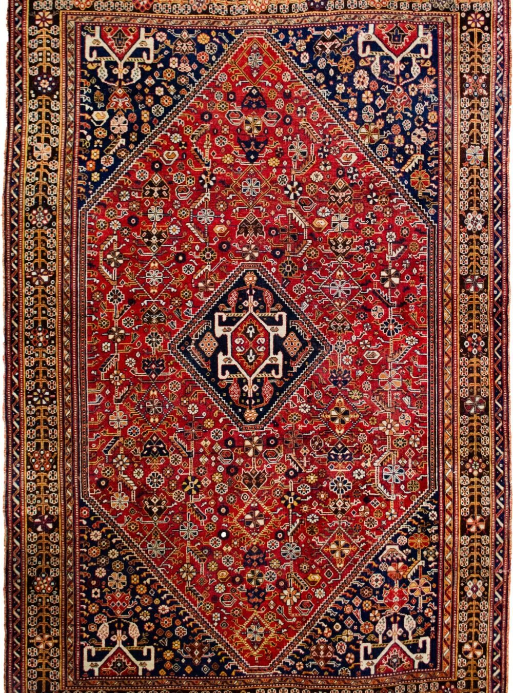 alt="Tribal rug with blue medallion and scarab beetle on terracotta ground" alt="Nomadic Persian rug with symbolic motifs and stylised border" alt="High-quality wool rug with tribal design and missing end knots" alt="Terracotta field tribal carpet with blue medallion and shrub border"