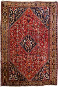 alt="Tribal rug with blue medallion and scarab beetle on terracotta ground" alt="Nomadic Persian rug with symbolic motifs and stylised border" alt="High-quality wool rug with tribal design and missing end knots" alt="Terracotta field tribal carpet with blue medallion and shrub border"